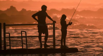 Silhouetteofmanandgirlfishingduringsunset